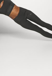 Sujetador deportivo negro con el logo de Puma, combinado con leggings negros de tiro alto que presentan acentos tonales y detalles de costura.