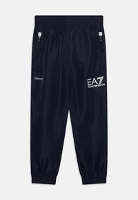 Pantalons de sport bleu marine en tissu lisse et léger. Dotés d'une taille élastique, de poches latérales zippées et d'accents de logo blanc.