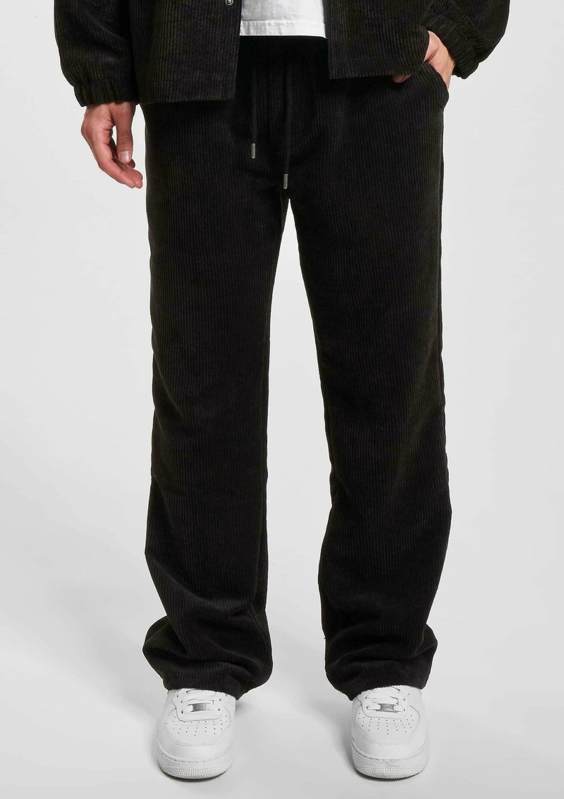 Sort fløjl bukser med løs pasform, der har snor i taljen og sidelommer, sat sammen med hvide sneakers.