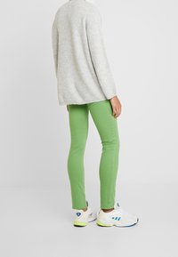 Grüne skinny Jeans kombiniert mit einem hellgrauen, strukturierten Strickpullover und weißen Sneakers mit blauen Akzenten und neongelben Sohlen.