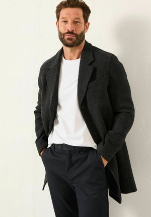 Charcoal wool blend coat with notched lapels, front pocket, paired with a white crew neck t-shirt and navy trousers. Smooth texture, tailored fit.
