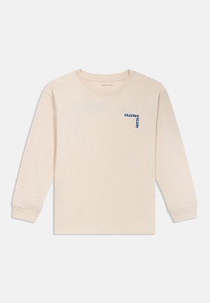 Krem majica s dugim rukavima od pamuka, s malim plavim logotipom "Calvin Klein" na lijevoj strani prsnog područja. Standardni dizajn s okruglim izrezom.