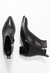 Czarne skórzane botki za kostkę z ostrymi noskami, bocznymi zamkami i niskimi blokowymi obcasami ułożone na białym tle.