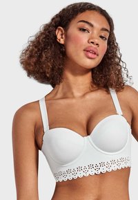 Sostén blanco acolchado con un diseño estructurado, que cuenta con tirantes ajustables y un borde decorativo de encaje en el dobladillo. Textura suave en todo.