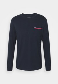 Marinblus med långa ärmar i bomull. Har en bröstficka med röda, vita och blå randiga detaljer. Slät textur och avslappnad passform.