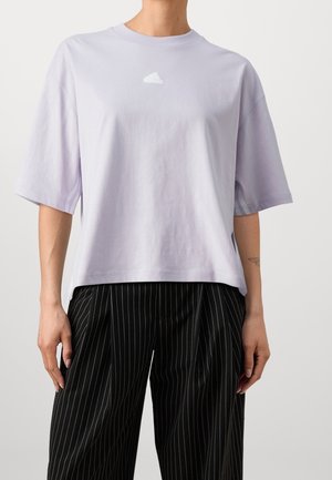 T-shirt en coton lilas à manches courtes et col rond, avec un petit logo blanc sur la poitrine. Associé à un pantalon noir à fines rayures.