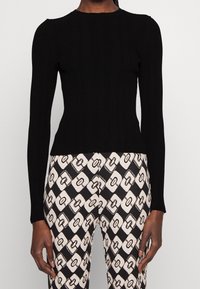 Czarny prążkowany top z długim rękawem o dopasowanym kroju. W zestawie z wzorzystymi spodniami w odcieniach czerni i kremu z motywem diamentów i łańcuchów.