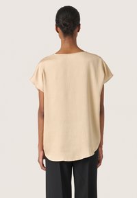 Beige, lätt blus med en texturerad yta, korta ärmar och rundad nederkant. Det mjuka tyget faller mjukt över kroppen.