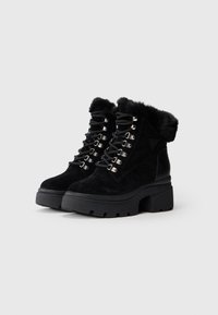Schwarze Wildleder-Stiefeletten mit Kunstfellfutter, mit metallischen Ösen, schwarzen Schnürsenkeln und einer klobigen Sohle.