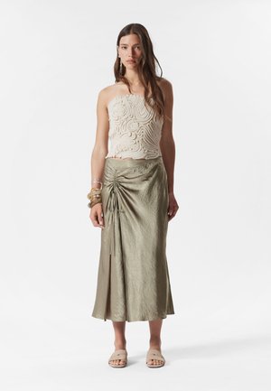 Beige textured crop top with swirling patterns and an olive green asymmetrical skirt featuring a drawstring detail. Flat sandals complete the look.