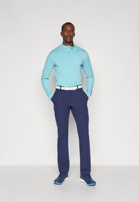 Jasnoniebieska koszulka polo z długim rękawem i pół-zamkiem, granatowe spodnie oraz niebieskie buty sportowe. Charakteryzuje się białym paskiem, dopasowanym krojem oraz gładką teksturą.