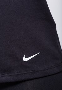 Musta kangas, jossa on valkoinen Nike-swoosh-logo brodeerattu helman lähelle, näyttäen hienoja ompelutietoja materiaalissa.