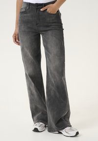 Wide-leg jeans in dark gray denim. Features a high waist, front pockets, and subtle faded texture. Paired with white athletic shoes.