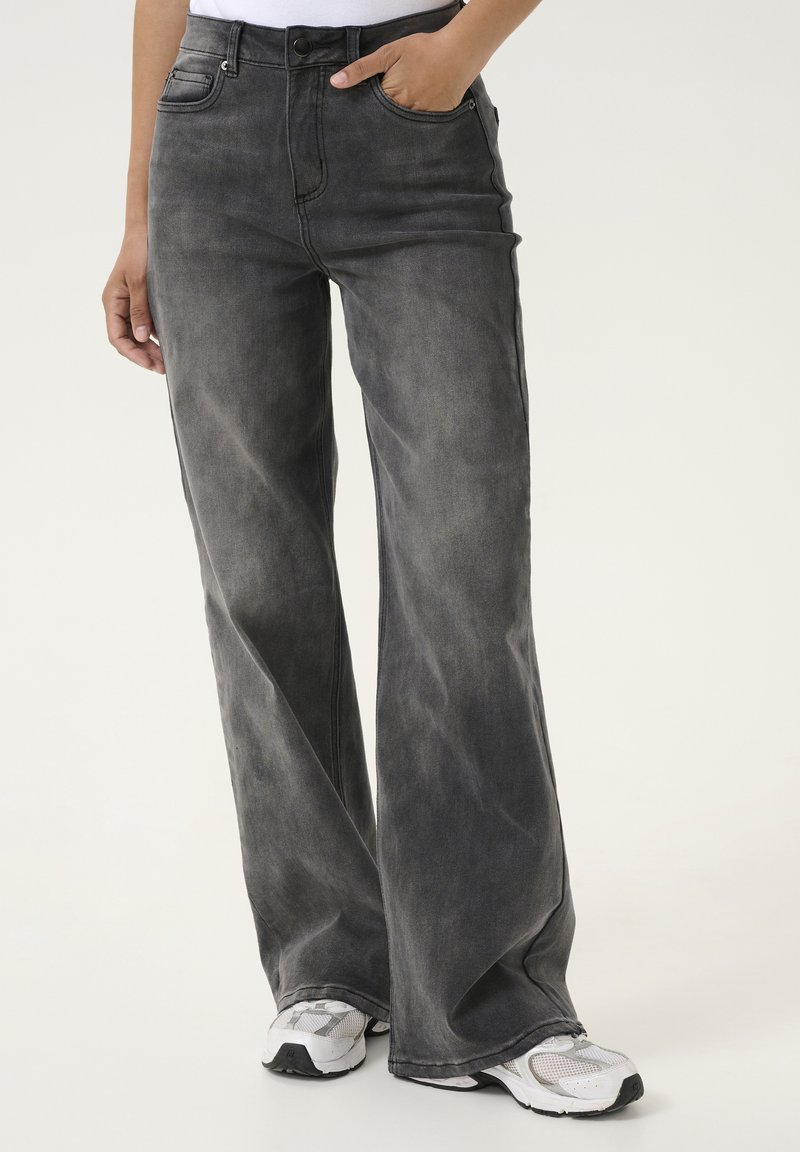 Wide-leg jeans in dark gray denim. Features a high waist, front pockets, and subtle faded texture. Paired with white athletic shoes.