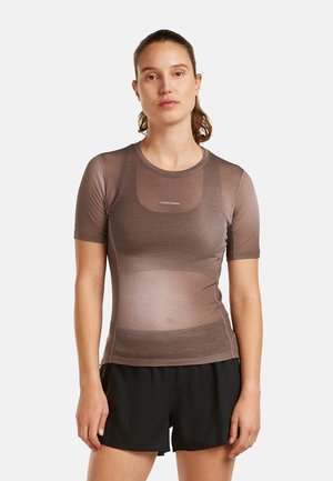 Femme debout, face à l'avant, portant un haut marron ajusté à manches courtes texturé et un short noir ample sur un fond blanc.