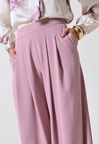Pantaloni plissettati rosa chiaro realizzati in tessuto morbido, con vita alta e tasche laterali, abbinati a una blusa a maniche lunghe floreale.