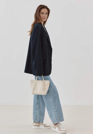 Marineblauer Oversized-Blazer, hellblaue weite Jeans, Taschen in Cremefarbe und cremefarbene Sneaker mit silbernen Akzenten. Sanfte Texturen und strukturiertes Design.