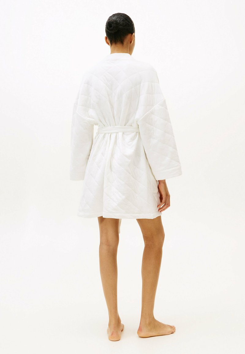 Witte gewatteerde badjas met lange mouwen, getailleerde taille en lengte tot halverwege de dijen. Heeft een gladde textuur en een subtiel diamantenpatroon.