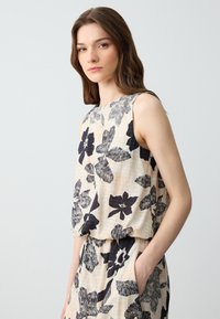 Top senza maniche a fantasia floreale color beige chiaro con fiori neri, caratterizzato da una vestibilità ampia e un tessuto morbido e strutturato.