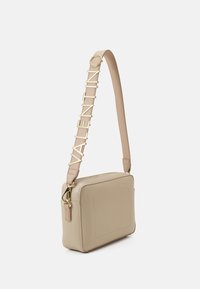 Beige rechthoekige leren handtas met een gestructureerde afwerking, voorzien van een strap met een gouden logo-accent en een ritssluiting voor gemakkelijke toegang.