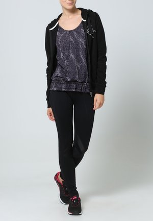 Zwarte zip-up hoodie, grijs patroon tanktop, en zwarte leggings en schoenen met roze accenten. Focus op het ontwerp en de pasvorm van actieve kleding.