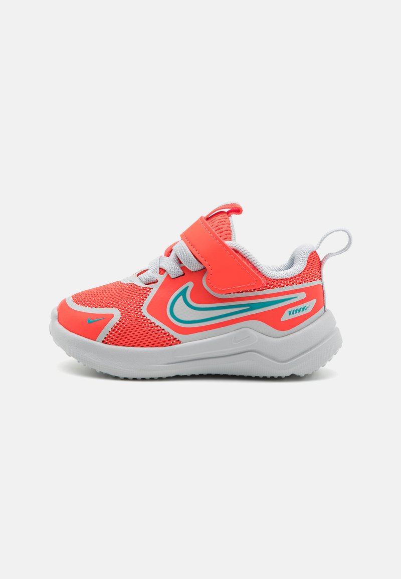 Chaussure de sport en maille rouge avec une sangle Velcro, semelle blanche, accents bleus et finition texturée. Présente un logo sur le côté et une languette à l'arrière.