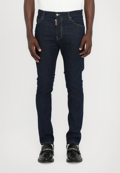 Dark blue denim jeans with a slim fit, five pockets, and gold stitching. Includes a textured waistband and a zipper fly with a button closure.