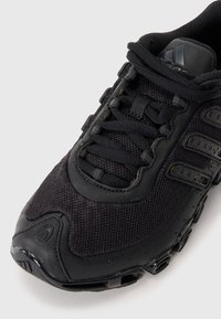 Sapatilha desportiva preta com um upper em malha texturizada, fecho de atacadores e sola de borracha elegante com acentos de ventilação.
