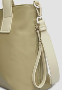 Beżowa torba tote o gładkiej skórzanej fakturze, z bocznym zamkiem błyskawicznym, regulowanym paskiem i logo wytłoczonym na pasku.