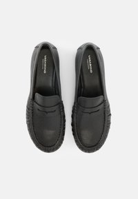 Ζευγάρι μαύρα δερμάτινα μοκασίνια χωρίς κορδόνια με στρογγυλεμένες μύτες, ραφές και την επιγραφή «Vagabond Shoemakers» στις εσωτερικές σόλες.