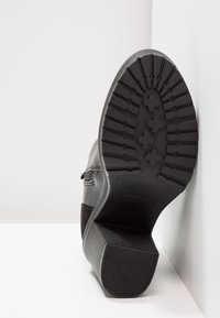 Stivale nero alla caviglia con suola in gomma texturizzata, caratterizzato da un motivo di battistrada robusto. Tomaia in pelle con zip laterale accentuata e tessuto morbido.