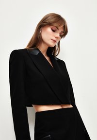 Svart kort blazer med glansiga svarta faux läderaxlar och en skräddarsydd design, kompletterad av en matchande kjol.