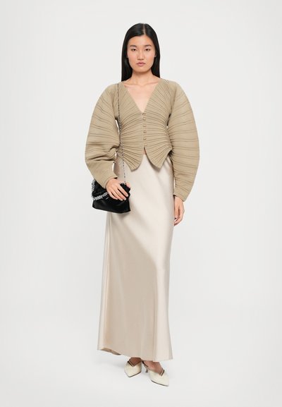 Beige ribbed crop cardigan with button closure, paired with a sleek satin light beige maxi dress and black purse with chain strap.