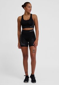 Svart atletisk crop top och högmidjade shorts i texturerat material med reflekterande detaljer, kombinerat med svarta sneakers.