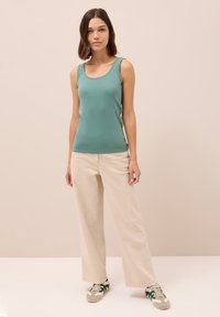 Canottiera verde con scollatura a girocollo, abbinata a pantaloni beige a gamba larga e sneakers verdi e grigi. Tessuto morbido, vestibilità casual.