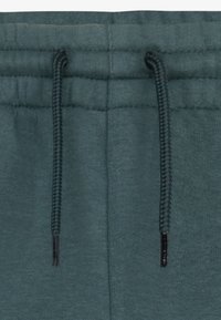 Close-up of dark green sweatpants waistband with matching drawstrings threaded through eyelets.