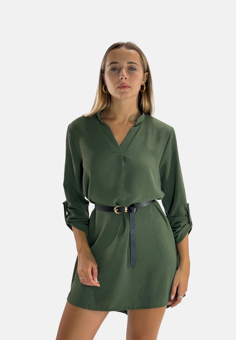 Abito verde a maniche lunghe con scollo a V e maniche arrotolabili, stretto in vita con una cintura nera con fibbia dorata. Tessuto morbido.