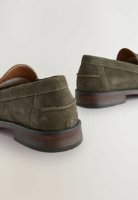 Donkergroene suede loafer met een ronde neus, gladde bruine leren voering en een gestructureerde houten hak. Stikdetails zijn zichtbaar.