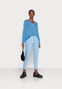 Blusa de manga longa azul floral, jeans de cintura alta azul claro, bolsa preta texturizada e sandálias pretas de plataforma com tiras.