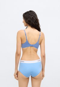Modrá podprsenka s nastavite ľnými ramienkami a jemnou, hladkou textúrou. Doplnok tvoria svetlomodré nohavičky s bielym pásom a detailom s logom.