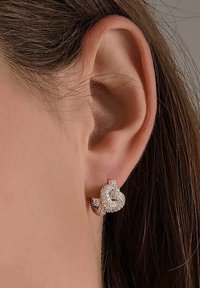 Orecchini a forma di cuore in oro rosa adornati con scintillanti pietre trasparenti, che mostrano una finitura metallica liscia e un design con chiusura sicura.
