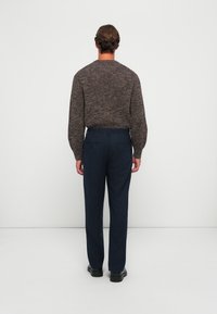 Textured brown knit sweater with long sleeves, paired with dark blue tailored pants and black shoes. Viewed from the back.
