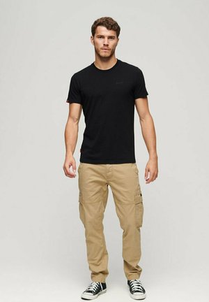 T-shirt nera in cotone con maniche corte, abbinata a pantaloni cargo beige. L'outfit presenta un design semplice e delle sneaker casual.