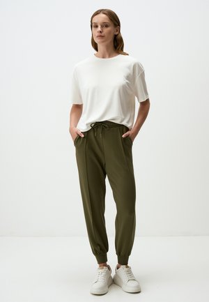 T-shirt bianca a maniche corte abbinata a pantaloni jogger verde oliva con vita regolabile e polsini elastici. Indossati con sneakers bianche.