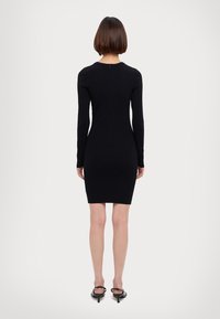 Black ribbed knit dress with long sleeves, bodycon fit, crew neckline, and a back zipper detail. Smooth texture and knee-length design.