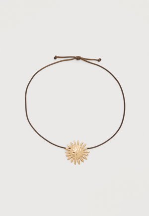 Barna állítható zsinór nyaklánc fényes arany színű, nap alakú medállal, amely szabálytalan sugarakkal rendelkezik, világos háttéren.