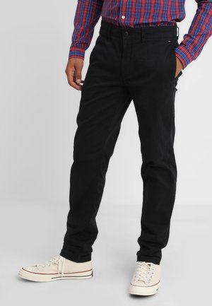 Zwarte katoenen broek met een rechte pijp, voorzien van een knoopsluiting, riemlussen en zijzakken. Gecombineerd met witte sneakers.