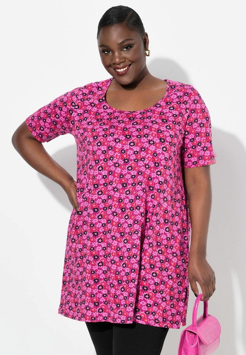 Rosa Blumen-Tunika mit kurzen Ärmeln, verziert mit schwarzen und roten Blumenmustern, kombiniert mit schwarzen Leggings und einer kleinen rosa Handtasche.