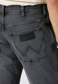 Czarne dżinsy o męskim kroju, z firmową skórzaną naszywką i charakterystycznym przeszyciem na tylnej kieszeni. Gładka faktura.