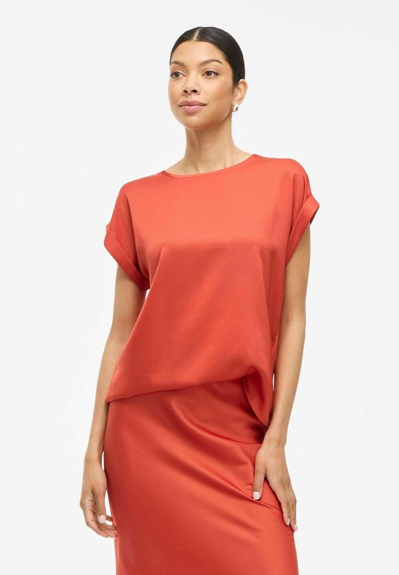 Rød satin top med rullede ærmer og en løs pasform. Glat tekstur og drapering, parret med en matchende satin nederdel. Minimalistisk design.